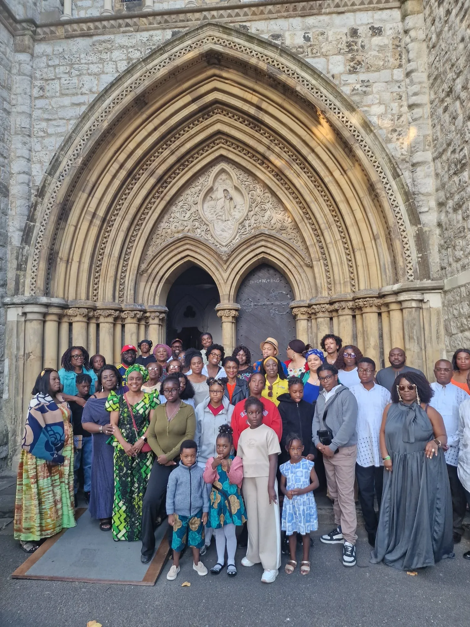 Members and families of all ages gathered in front of a carved church doorway at the Summer Get-Together 2026